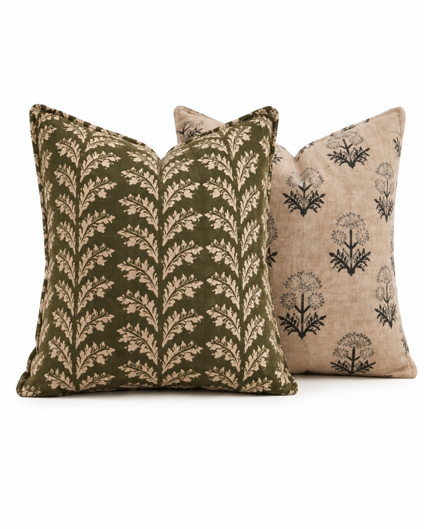 Set of 2 earthy designer cushion covers with botanical leaf and floral block print patterns in olive green and beige, styled on a luxury wooden sofa in a modern Indian living room.